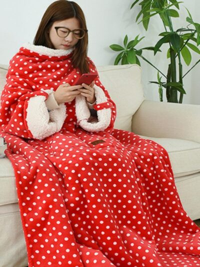 Femme brune assise sur un canapé beige avec une couverture rouge à pois blancs regardant son téléphone