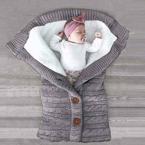 Bébé dans une couverture en laine grise, avec un turban rose et un body blanc