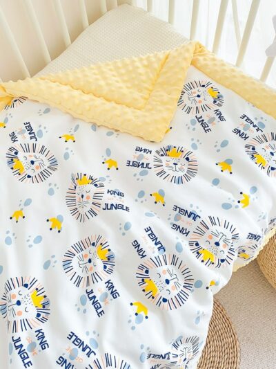Couverture avec des bords jaunes et des dessins de lions posée sur un lit de bébé
