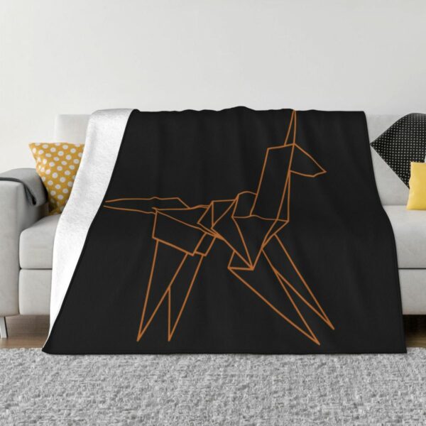 Couverture noire avec une licorne à forme géométriques dorées dessus, posée sur un canapé gris avec un tapis gris