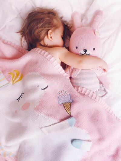 Enfant dans un lit dormant avec un doudou rose et une couverture rose avec une licorne dessus