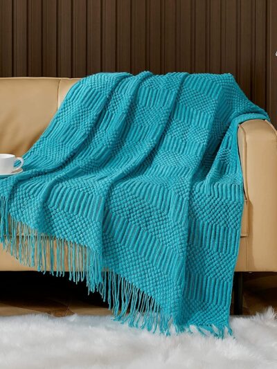 Canapé recouvert d'une couverture bleue à franges. On voit également une tapis.