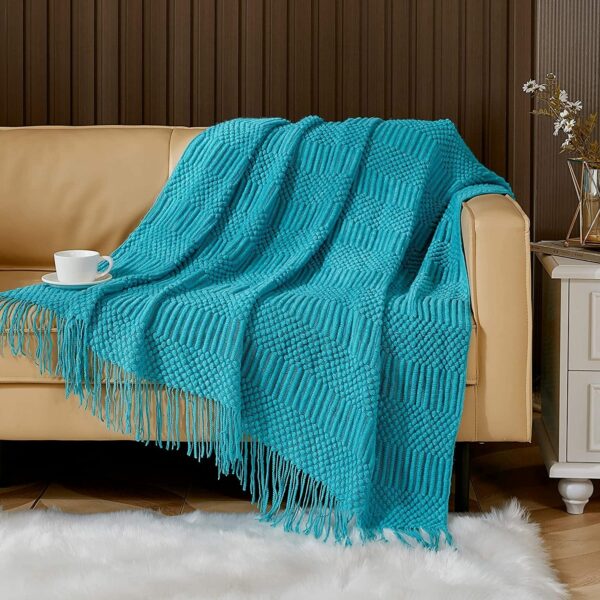 Canapé recouvert d'une couverture bleue à franges. On voit également une tapis.