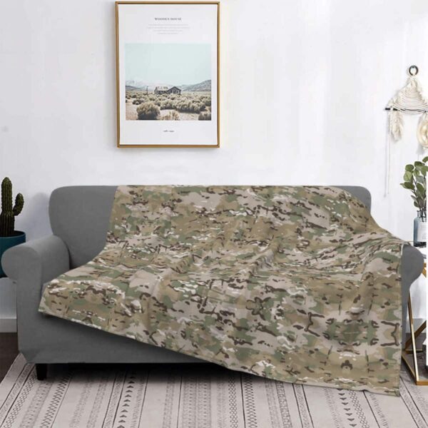 Couverture camouflage posée sur un canapé gris. On voit également un cadre.