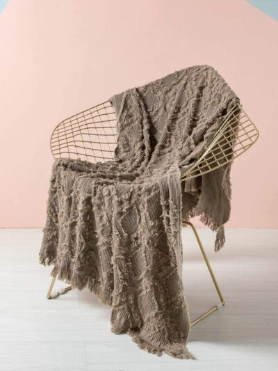 Photo d'une couverture marron en tricot style bohème sur une chaise sur un fond rose et gris