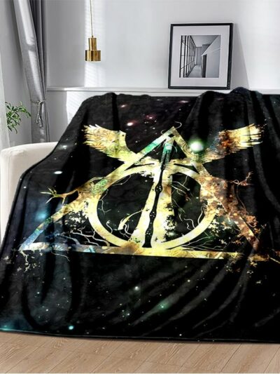 Couverture polaire Harry Potter noire avec le symbole des reliques de la mort posée sur un canapé beige dans un salon.
