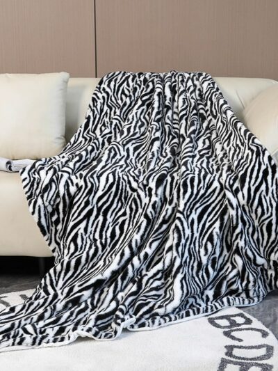 Photo d'une couverture n fausse fourrure imprimé zèbre posée sur un canapé beige, retombant sur un tapis blanc