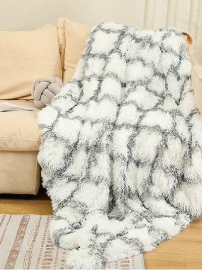 Photo d'une couverture en fausse fourrure blanche à carreau posé sur un canapé beige