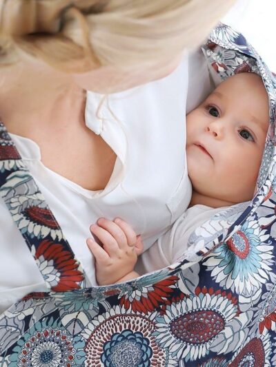 Bébé dans les bras d'une femme blonde avec une couverture à fleurs colorés entourée autour du bébé
