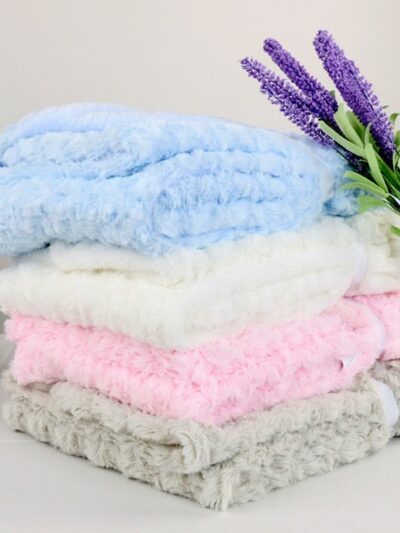 Photo de couvertures polaire colorées empilées avec de la lavande posée contre la pile de couvetures. Les couvertures ont un effet de champs de rose avec leur tissage floral.