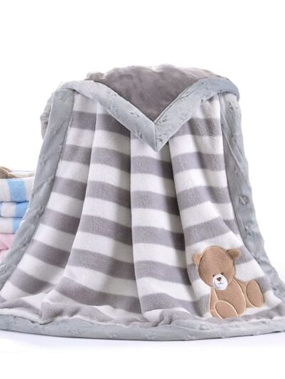 Photo d'une couverture polaire pour bébé gris à rayure avec un petit ourson dans le coin en bas à droite.