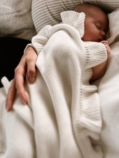 On voit un nouveau-né qui est allaité dans une couverture en maille blanche à volant très jolie.