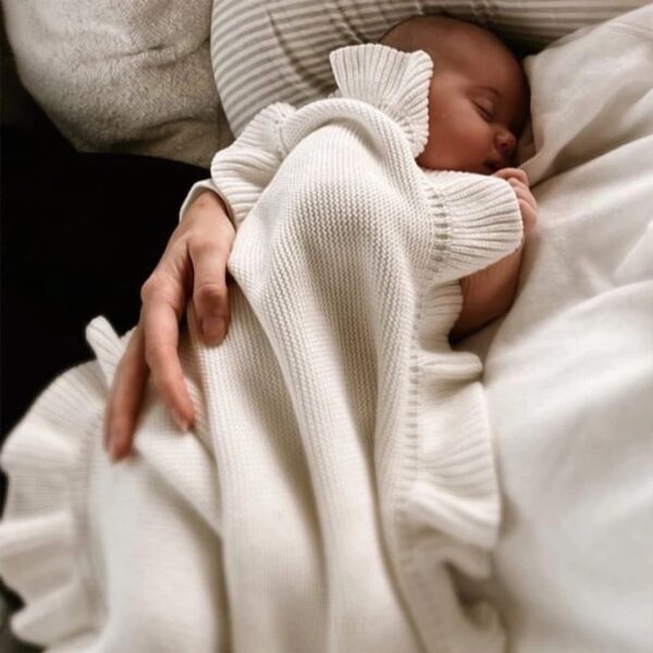 On voit un nouveau-né qui est allaité dans une couverture en maille blanche à volant très jolie.