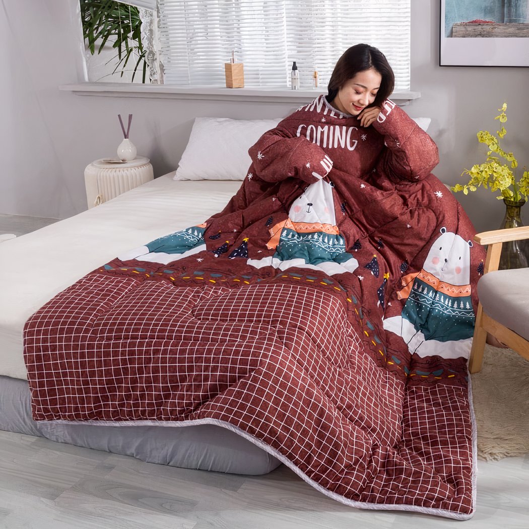 Femme assise dans un lit blanc avec une couverture marrons à motifs d'ours blancs.