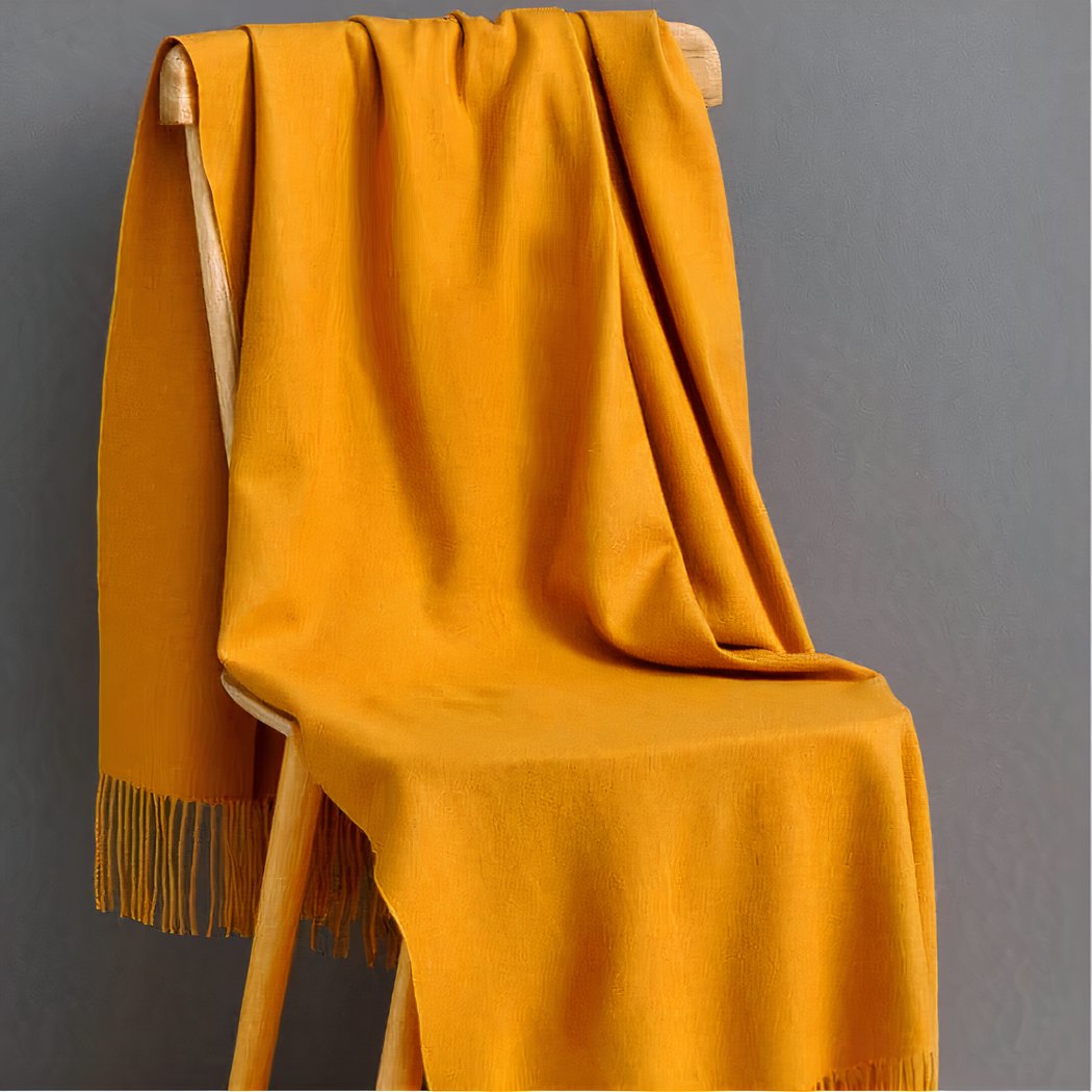 couverture jaune en laine à franges posée sur une chaise en bois