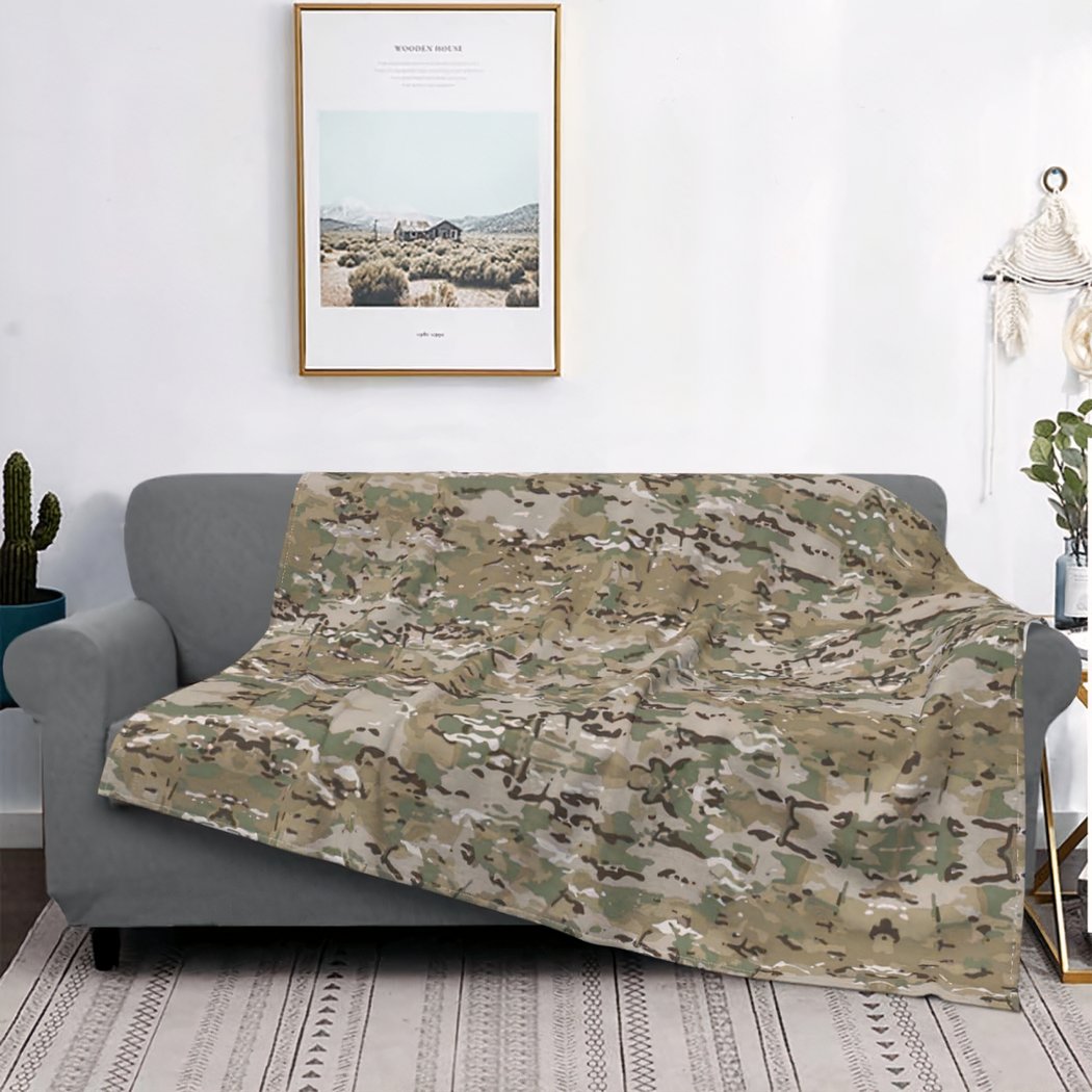 Couverture camouflage posée sur un canapé gris. On voit également un cadre.