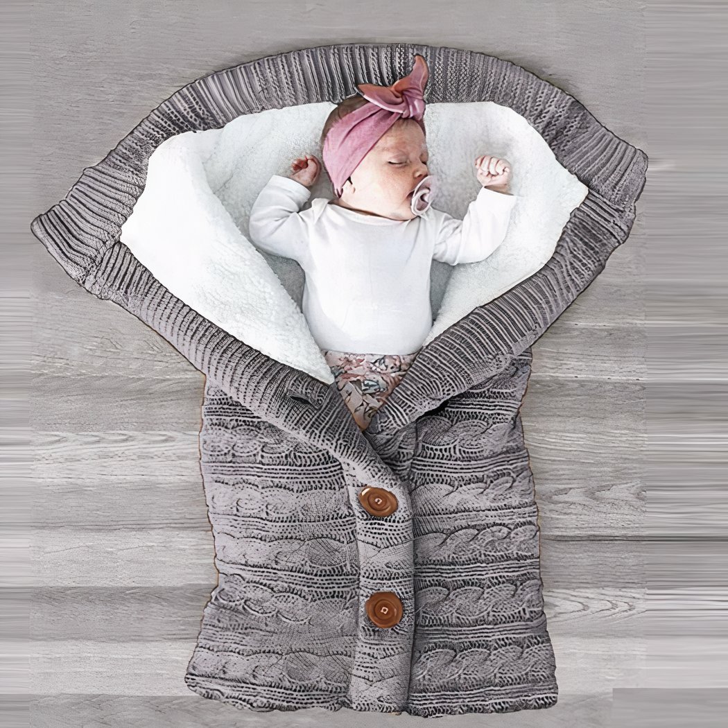 Bébé dans une couverture en laine grise, avec un turban rose et un body blanc