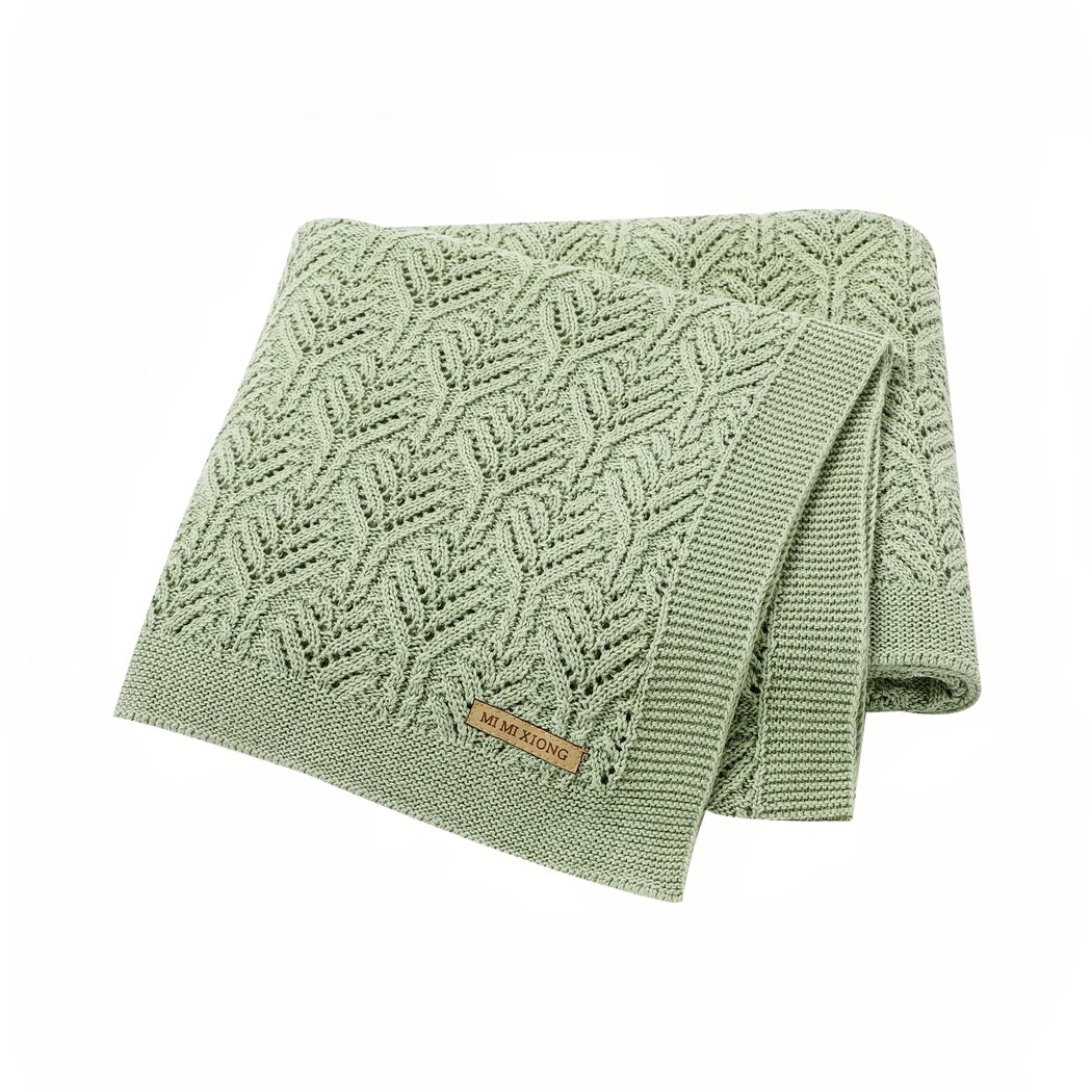 On voit une superbe couverture en tricot dont les mailles sont en forme de feuilles. Elle est verte et vraiment jolie.