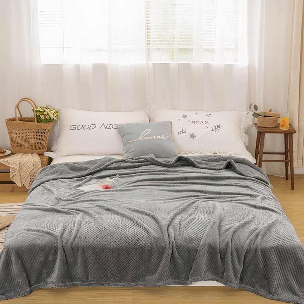 Canapé recouvert d'une couverture grise, on voit aussi des oreillers blancs et une fenêtre.