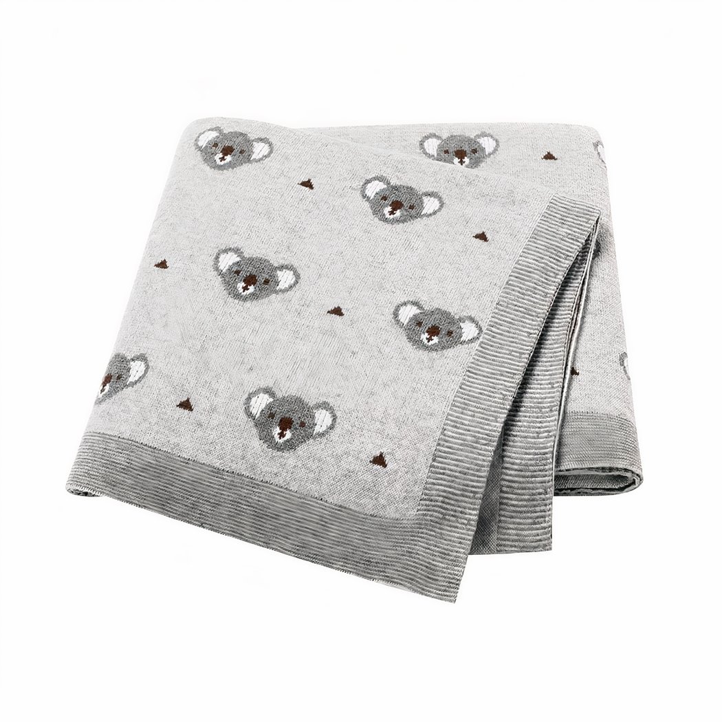 On voit une couverture pilée en quatre sur fond blanc. Elle est grise et ornée de têtes de koalas.