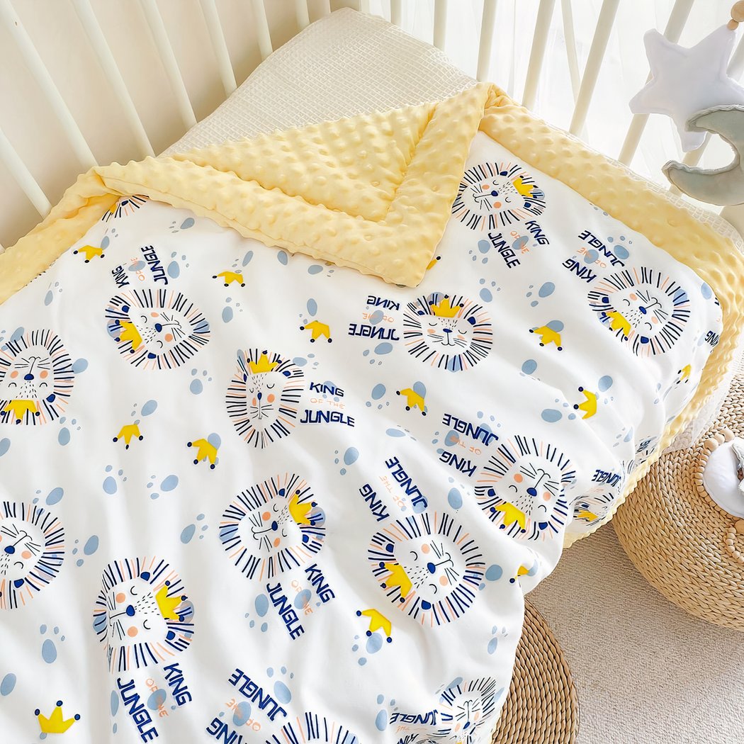 Couverture avec des bords jaunes et des dessins de lions posée sur un lit de bébé