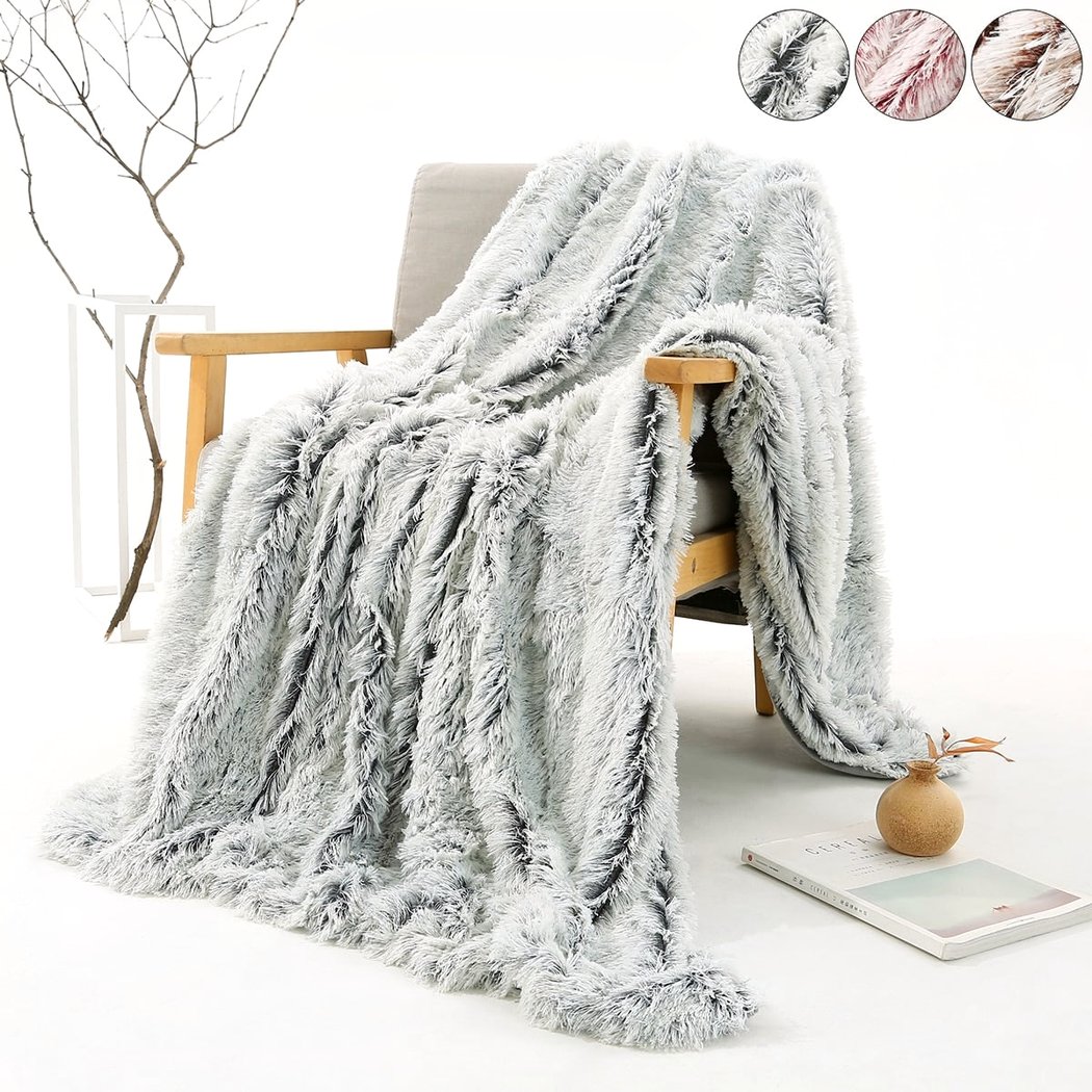 Photo d'une couverture en fausse fourrure grise posée sur une chaise avec un fond zen, proposition de plusieurs couleurs.