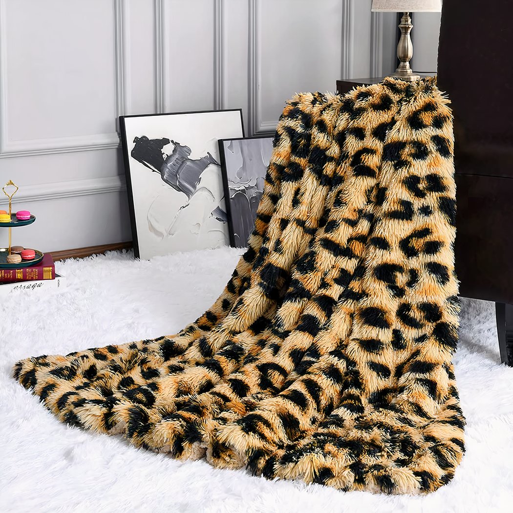 Photo d'une couverture en fausse fourrure imprimé léopard. La couverture est posé sur l'accoudoir d'une petite chaise et tombe sur un tapis en fausse fourrure blanche.