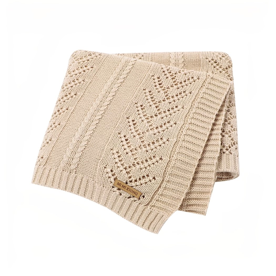 On voit une couverture en tricot beige avec des mailles ajourées, genre mailles pointelles. La couverture est pliéee en quatre et présentée sur fond blanc. C'est une couverture pour bébé, une jolie pièce.