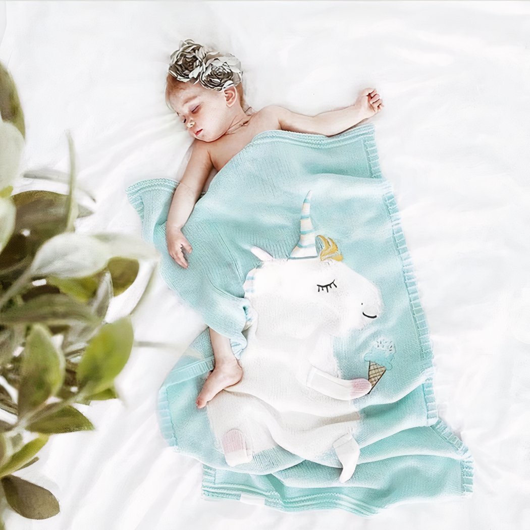 Enfant endormi dans une lit avec des draps blancs et une couverture bleue avec une licorne blanche dessus