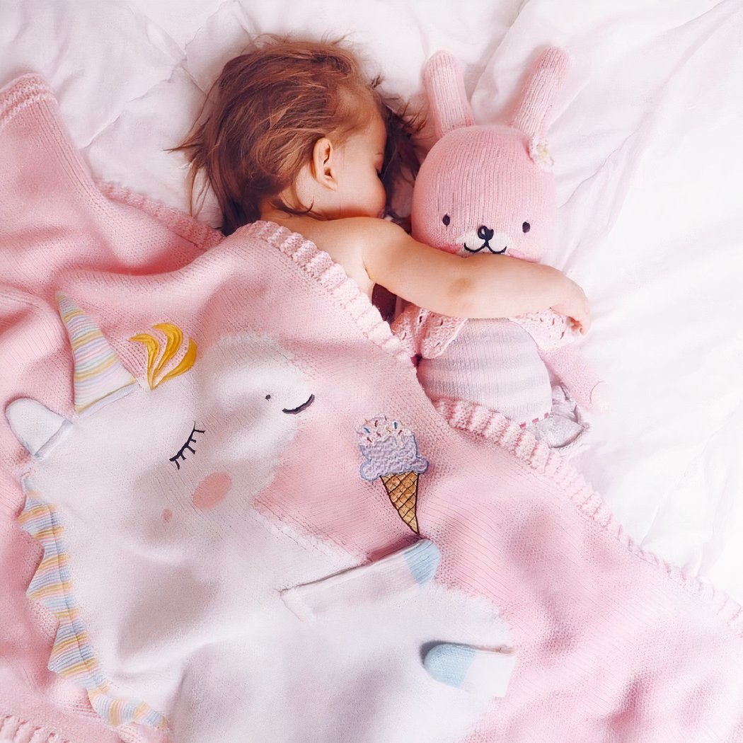 Enfant dans un lit dormant avec un doudou rose et une couverture rose avec une licorne dessus