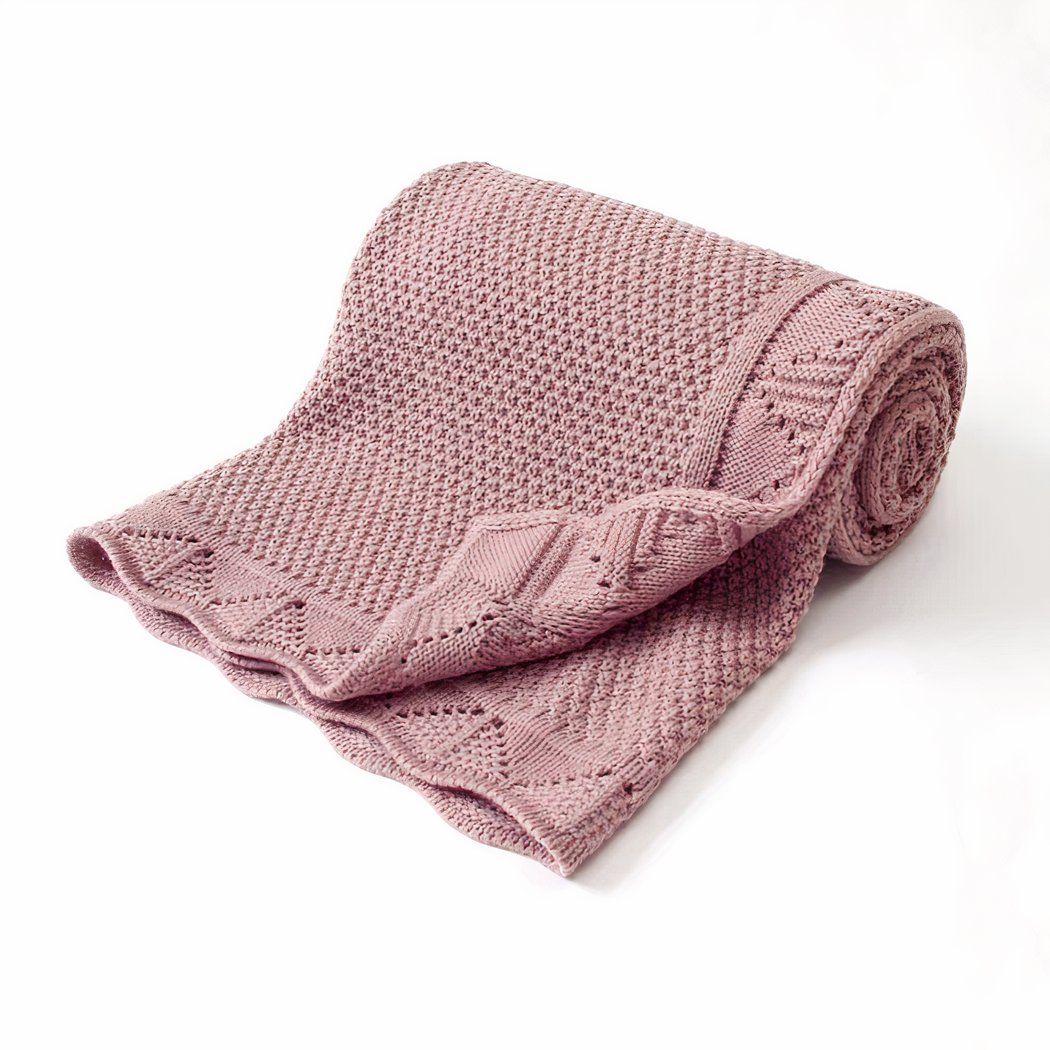 On voit une très jolie couverture en mailles tricotées pour bébé de couleur violet. Elle est enroulée sur elle-même et présentée sur fond blanc.