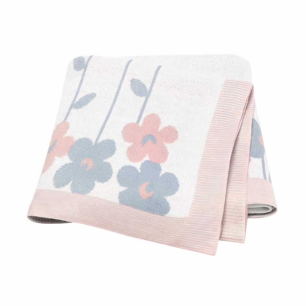 On voit une couverture pour bébé d'aspect vintage avec des motifs fleuris. La bordure est rose et l'intérieur blanc.