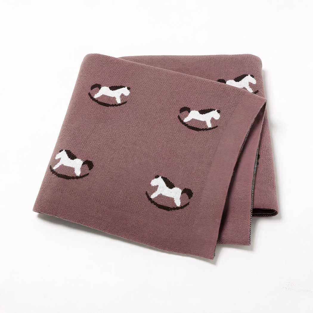 On voit une couverture pliée en quatre, marron, présentée sur fond blanc. Elle est ornée de petits chevaux à bascule.