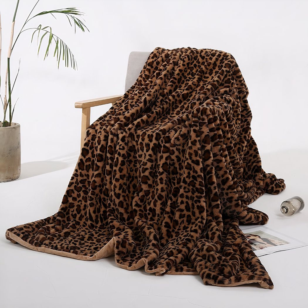 Photo d'une couverture en fausse fourrure léopard marron posée sur une chaise dans un décor minimaliste avec une petite plante dans le fond.
