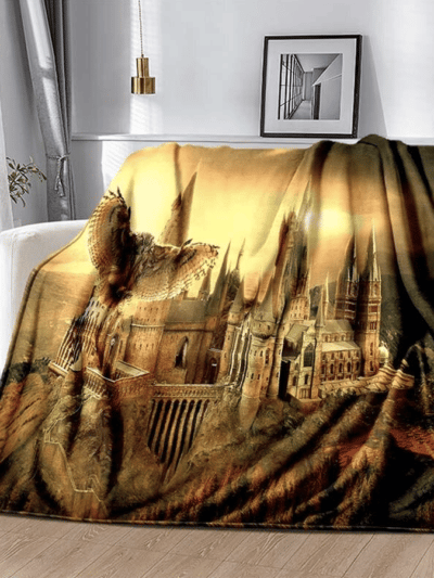 Couverture Harry Potter du château de Poudlard de jour avec un hibou. LA couverture est posée sur un fauteuil blanc dans un salon moderne.