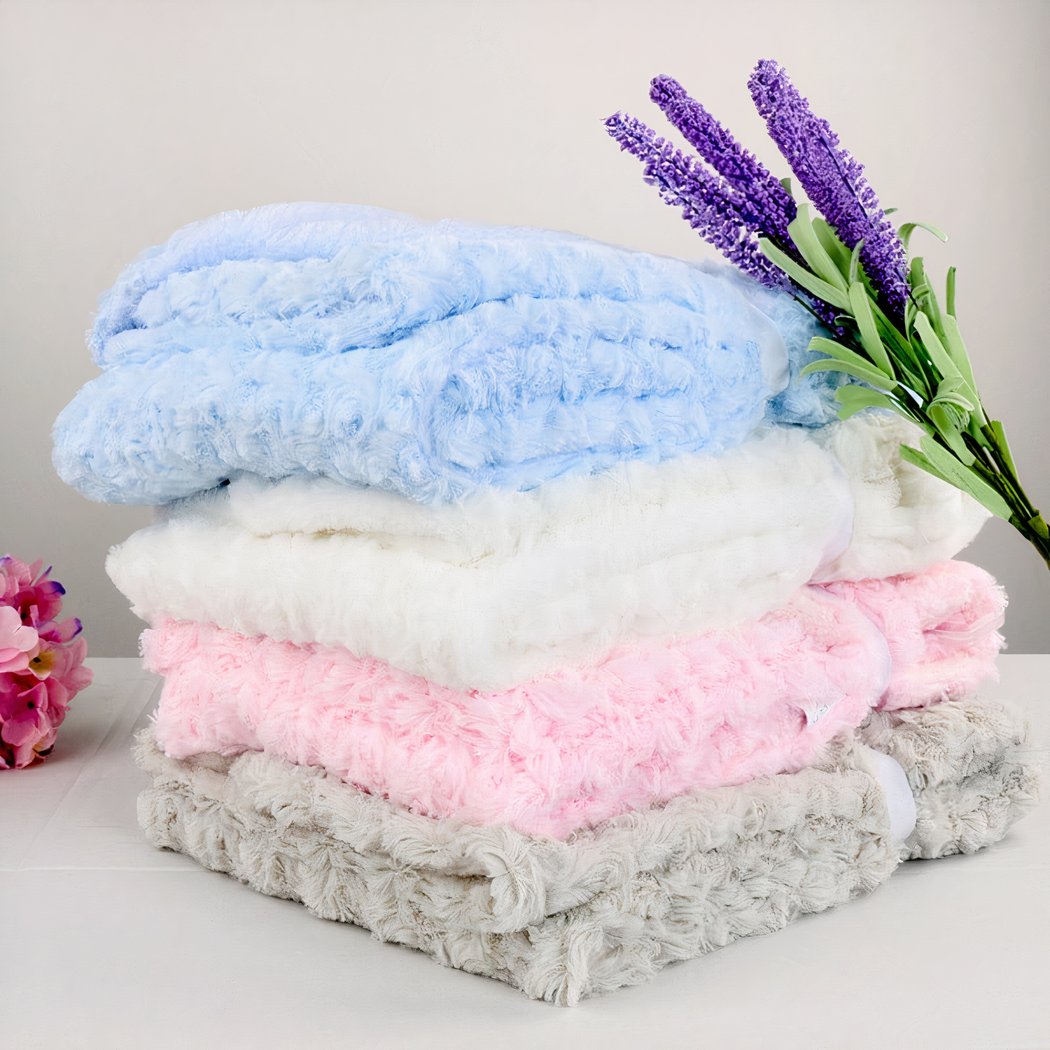 Photo de couvertures polaire colorées empilées avec de la lavande posée contre la pile de couvetures. Les couvertures ont un effet de champs de rose avec leur tissage floral.
