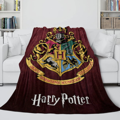 Couverture polaire rouge Harry potter avec le blason des quatre maisons posée sur un canapé blanc.