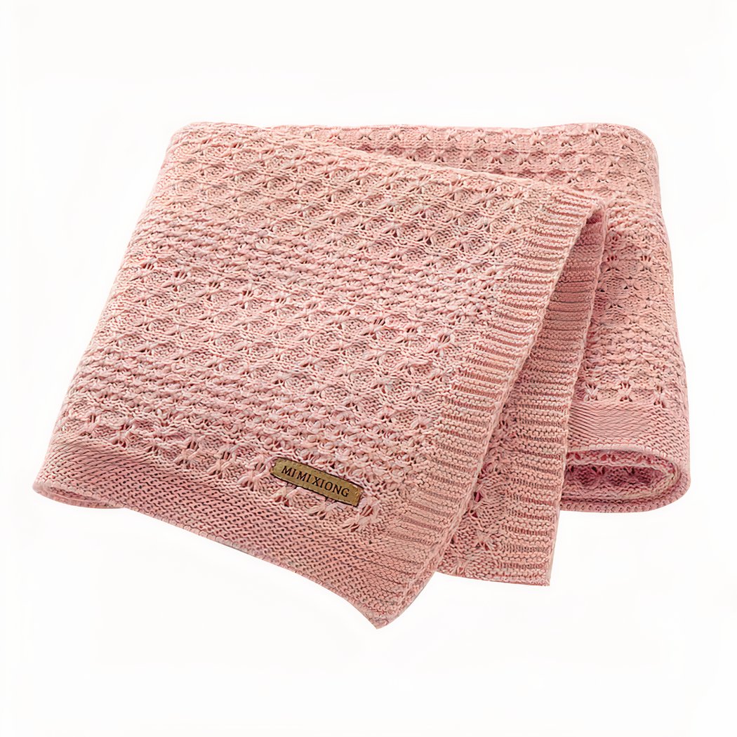 On voit une couverture rose en mailles tricotées. Elle est présentée sur fond blanc.