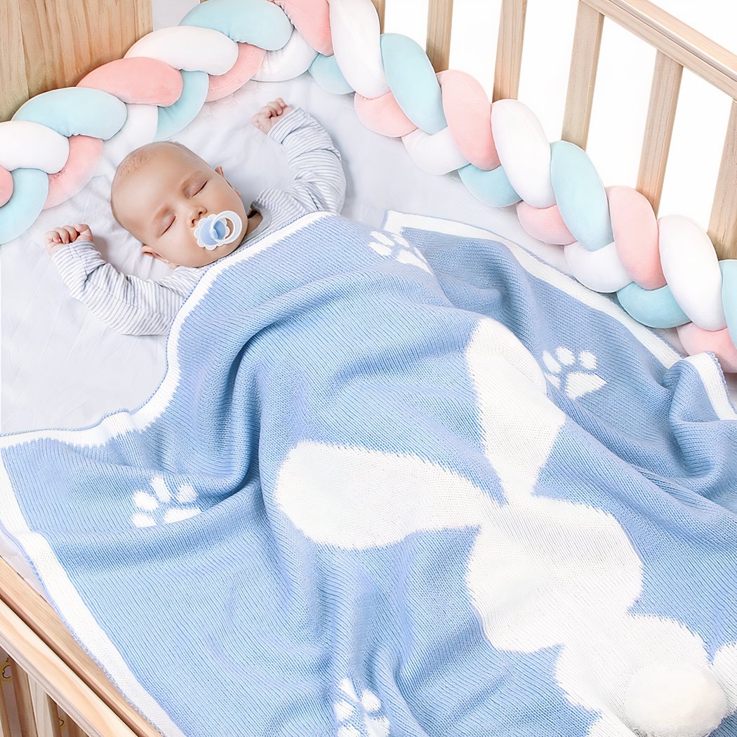 Bébé avec une tétine dormant dans un lit avec une couverture bleu avec un lapin blanc dessus.