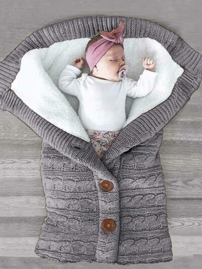 Bébé enveloppé dans une couverture tricotée en crochet de couleur grise.