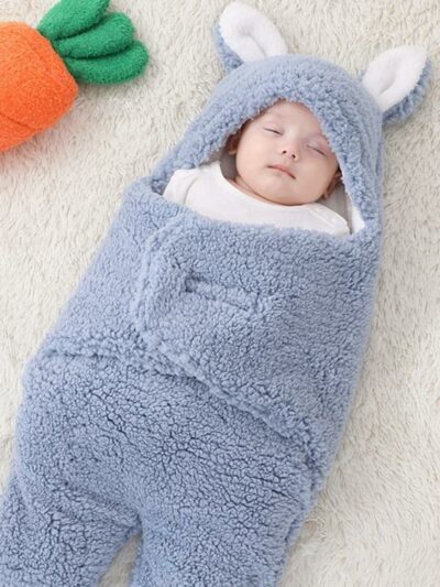 Enfant enveloppé dans une couverture bleue avec des oreilles de lapin et se trouvant à côté d'un doudou en forme de carotte