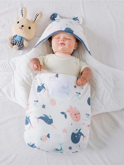 Poupée dans une couverture blanche à motifs baleines roses et bleues avec un doudou à côté de la tête du bébé.