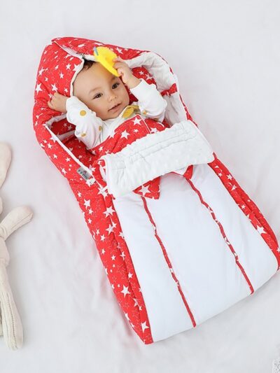 Bébé dans une couverture rouge et blanche à capuche avec un doudou à côté