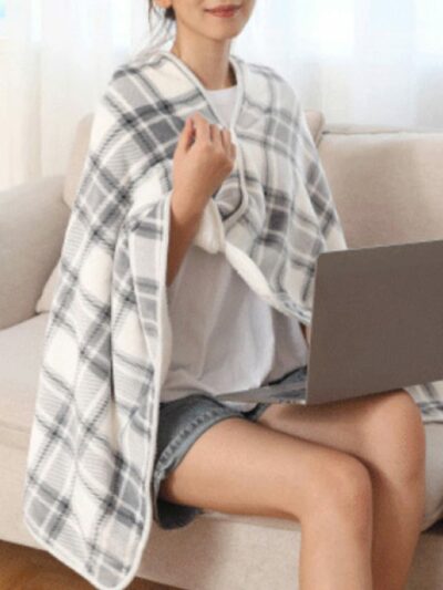 Femme portant une couverture à carreaux gris et étant assise sur un canapé avec un ordinateur sur les genoux.
