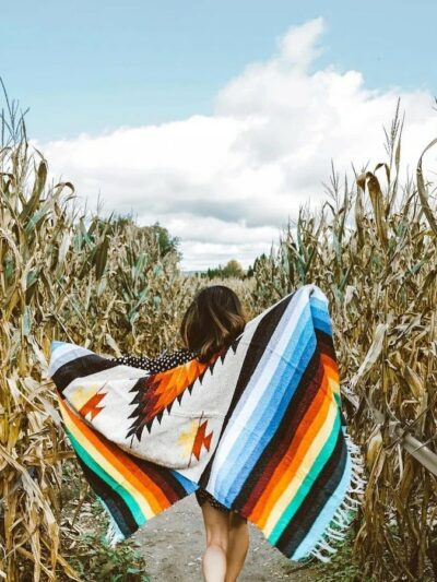 Photo d'une personne se baladant dans des champs de mais avec une couverture mexicaine colorée.