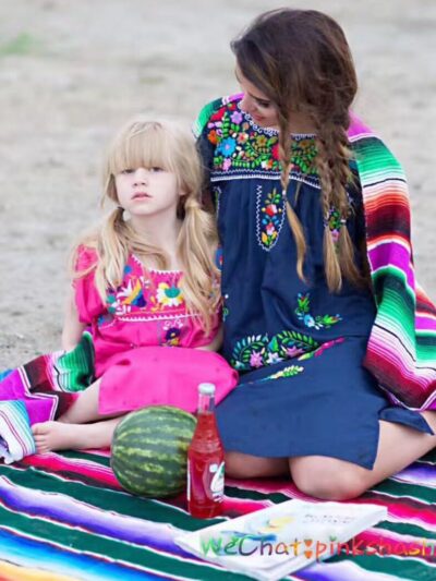 Photo d'une femme et son enfant assises sur la plage sur une couverture mexicaine multicolore avec des couvertures sur les épaules