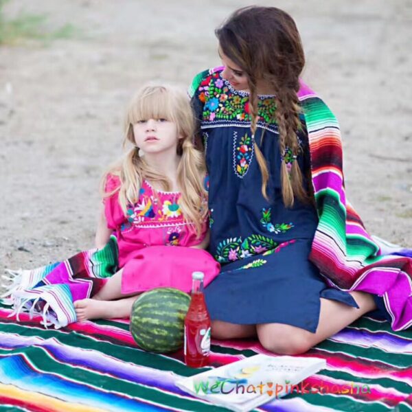 Photo d'une femme et son enfant assises sur la plage sur une couverture mexicaine multicolore avec des couvertures sur les épaules