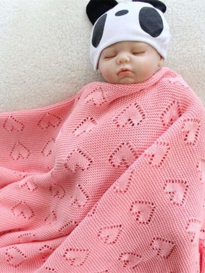 Faux bébé envelopper dans une couverture en forme de cœur tricotée en crochet de couleur rose.