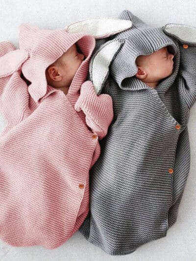 Nouveaux-nés emmaillotés dans une couverture tricotée en crochet de couleur grise et rose.
