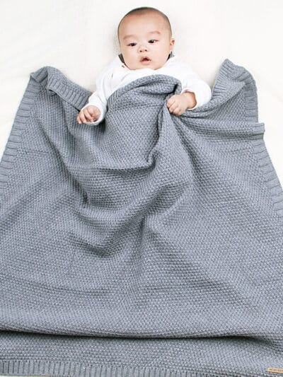 Bébé enveloppé dans une couverture tricoté en crochet de couleur grise.